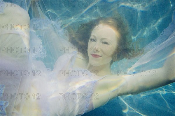 Caucasian woman wearing dress swimming underwater