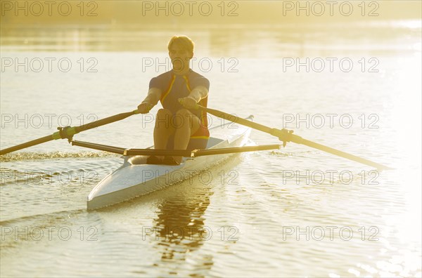 Caucasian man rowing on river at sunset