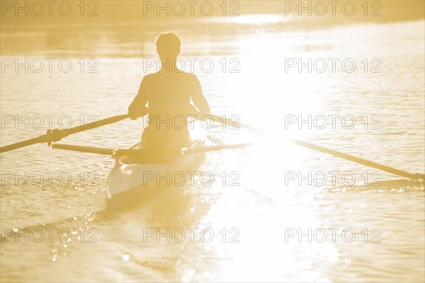 Caucasian man rowing on river at sunset