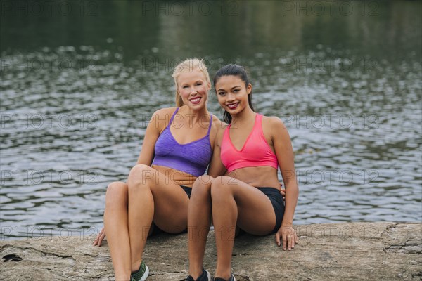 Portrait of smiling women sitting on log near lake