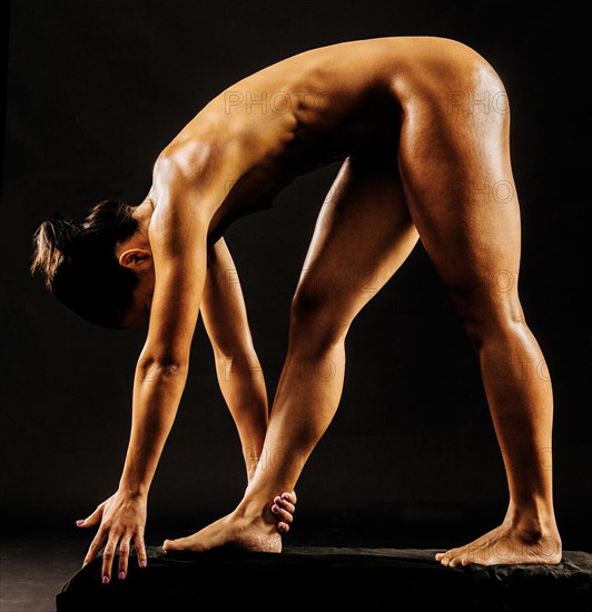Naked muscular Mixed Race woman bending and holding ankle