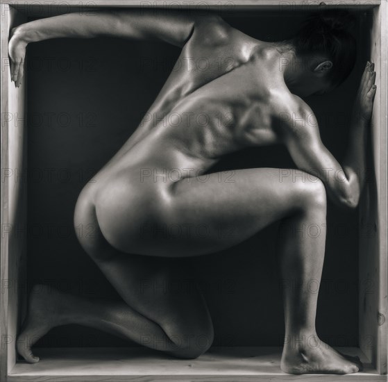 Naked muscular Mixed Race crouching in box