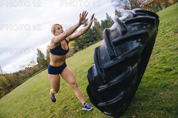Caucasian woman pushing heavy tire up hill