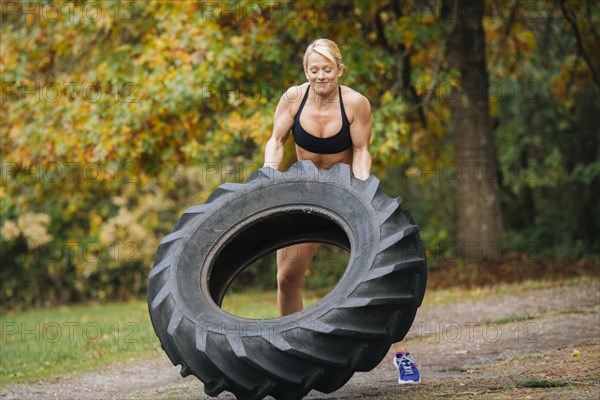 Caucasian woman lifting heavy tire in park