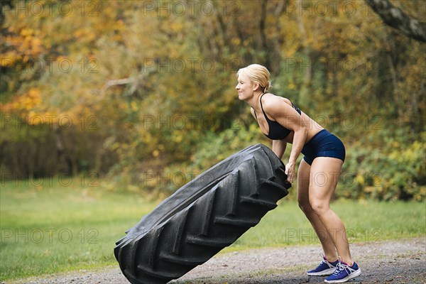 Caucasian woman lifting heavy tire in park