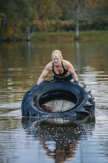 Caucasian woman lifting heavy tire in lake