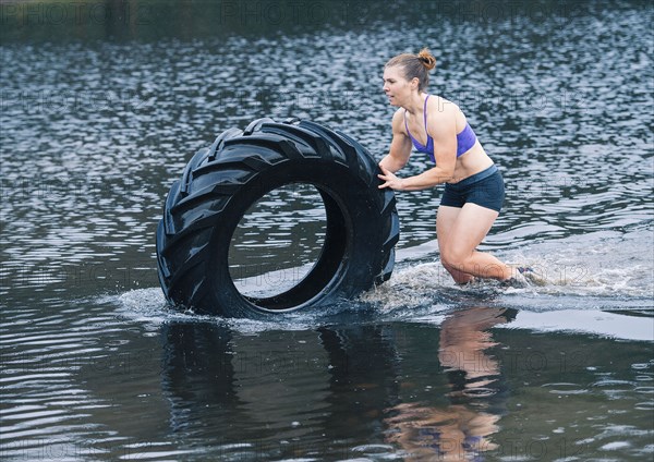 Caucasian woman pushing heavy tire in lake