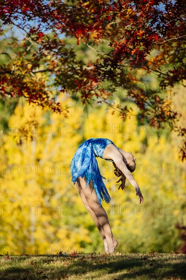 Caucasian ballerina dancing under branches in park