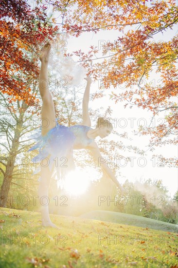 Back lit Caucasian ballerina dancing under branches in park