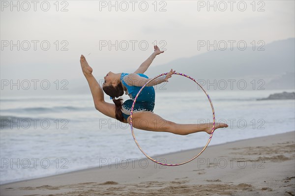 Caucasian gymnast jumping with hoop on beach