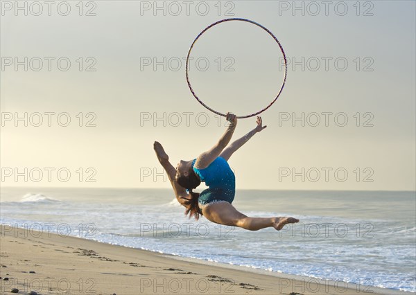 Caucasian gymnast jumping with hoop on beach