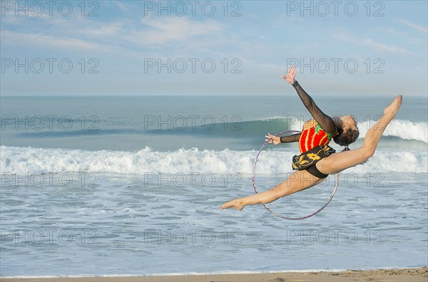 Caucasian gymnast jumping with hoop on beach