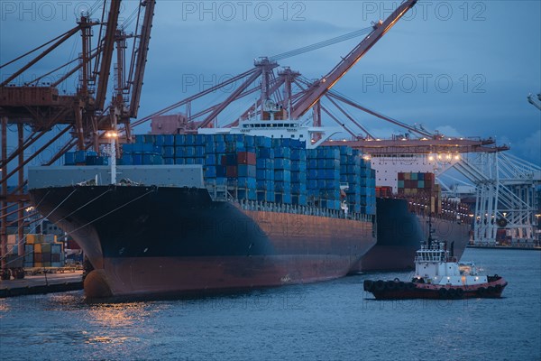 Cargo containers on freighter at shipping port near tugboat