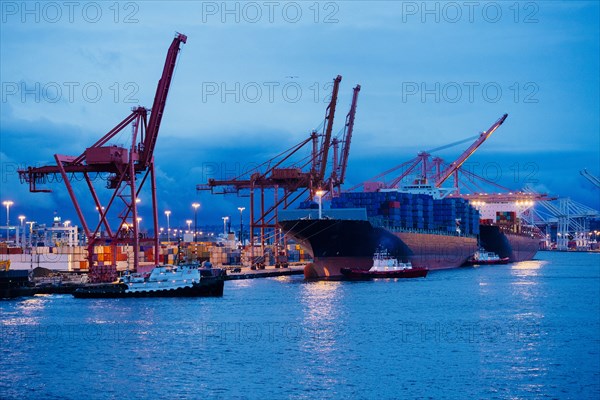 Cargo containers on freighter at shipping port near tugboats