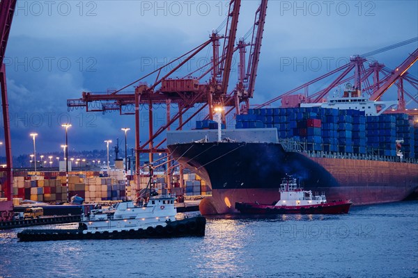 Cargo containers on freighter at shipping port near tugboats