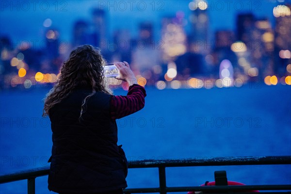 Caucasian woman on boat photographing urban waterfront with cell phone