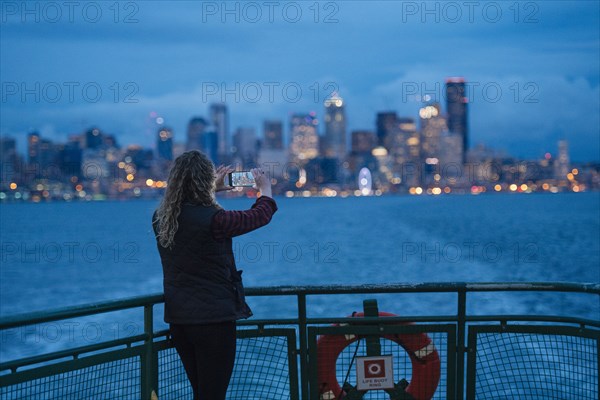 Caucasian woman on boat photographing urban waterfront with cell phone