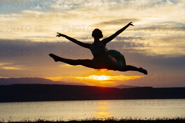 Caucasian ballerina jumping on beach at sunset