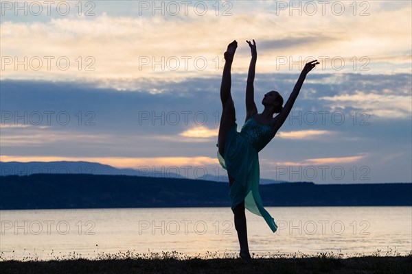 Caucasian ballerina dancing on beach at sunset