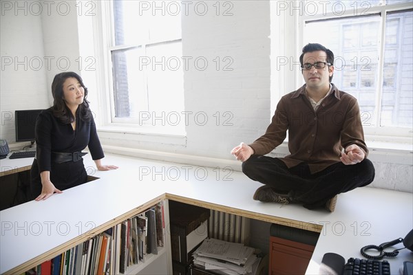 Hispanic businessman meditating next to coworker