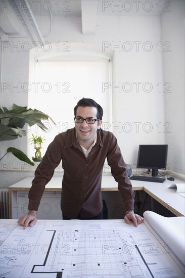 Hispanic businessman leaning on blueprints