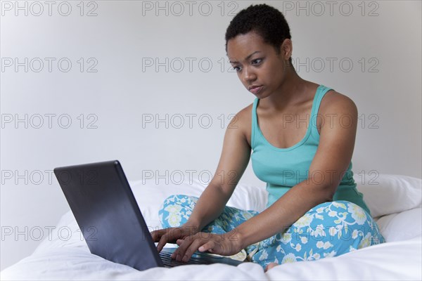 African American woman using laptop in bed