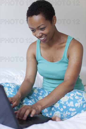 African American woman using laptop in bed