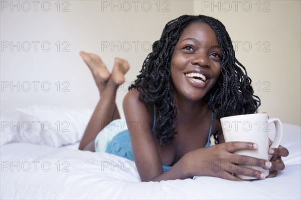 Black woman laying on bed drinking coffee