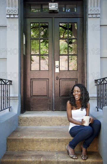 Black woman drinking coffee on front stoop