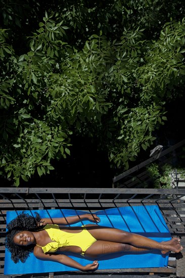 Black woman sunbathing on fire escape