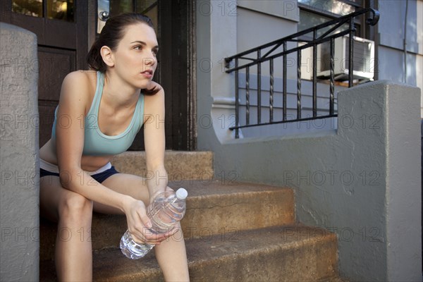 Caucasian woman relaxing with water bottle after exercise