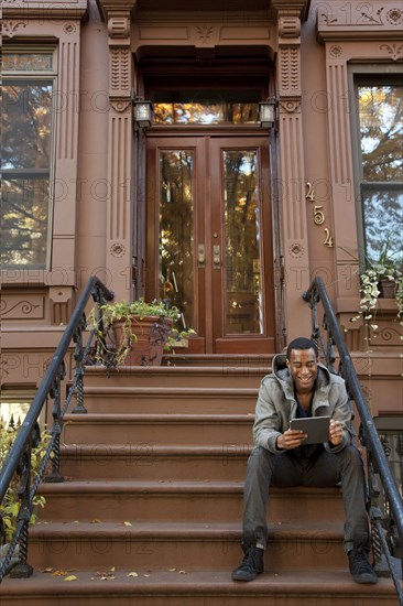 Black man sitting on front stoop using digital tablet