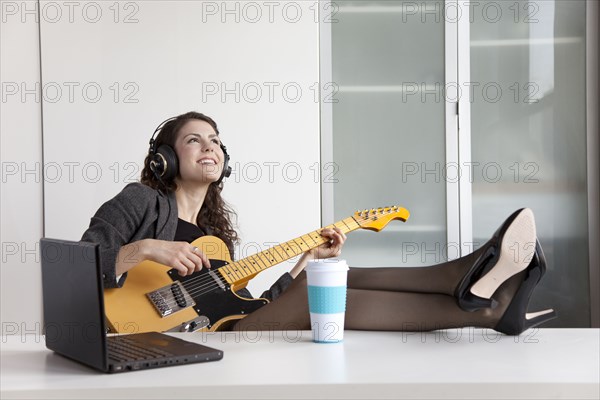 Businesswoman playing guitar at desk