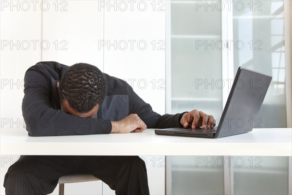 Tired Black businessman sleeping near laptop