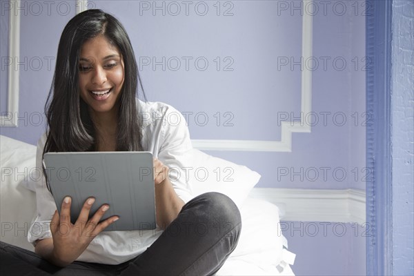 Sri Lankan woman on bed using digital tablet