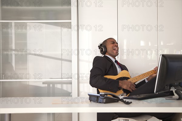 Black businessman playing guitar at desk
