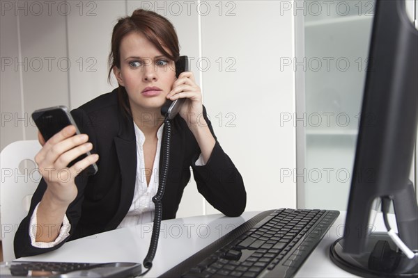 Businesswoman holding cell phone and talking on landline phone