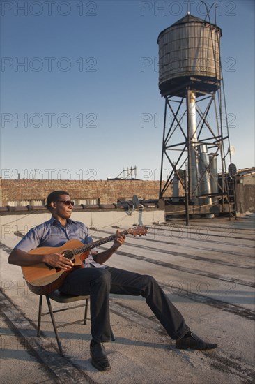 Black man playing guitar on rooftop