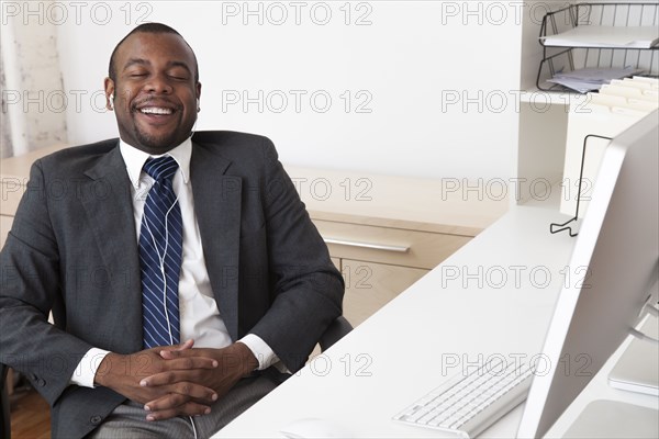 Black businessman listening to music at desk in office