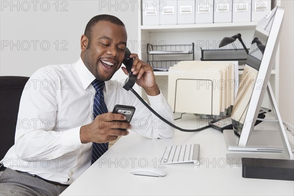 Black businessman using two telephones at one time