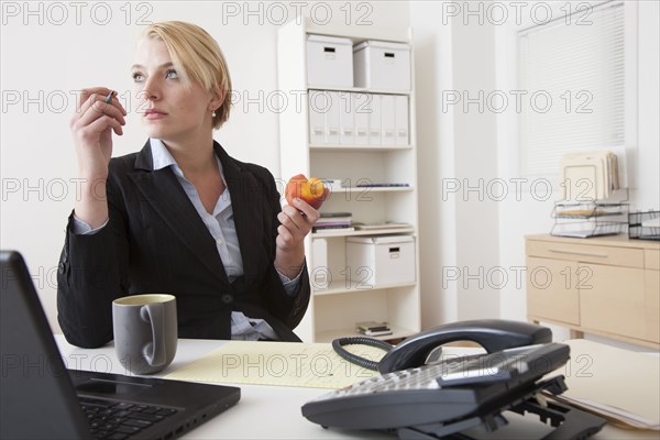 Caucasian businesswoman eating at desk in office