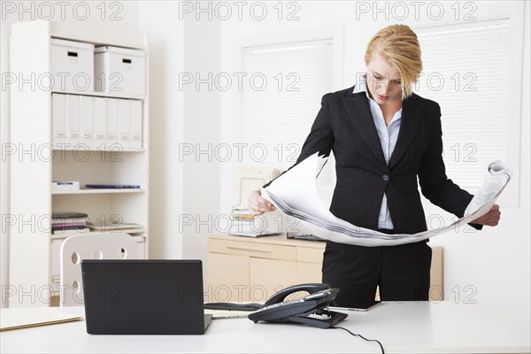 Caucasian businesswoman reading blueprints in office