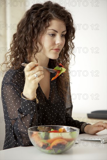 Caucasian businesswoman eating salad at desk