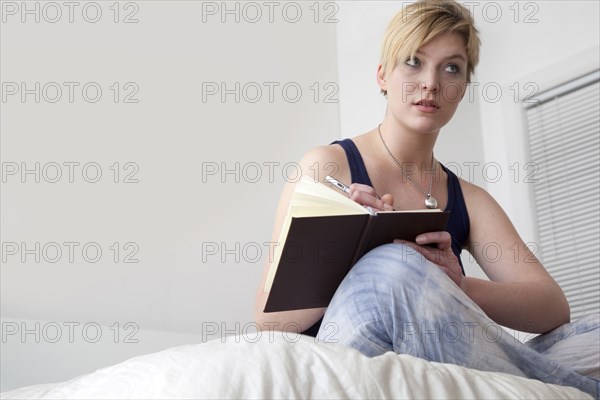 Caucasian woman writing in diary on bed