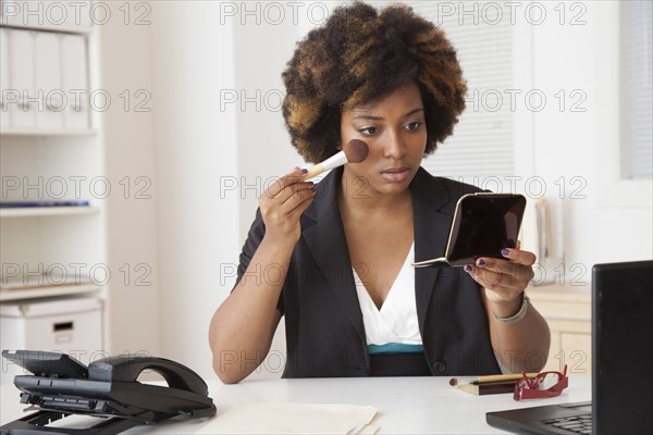 African American businesswoman applying makeup in office