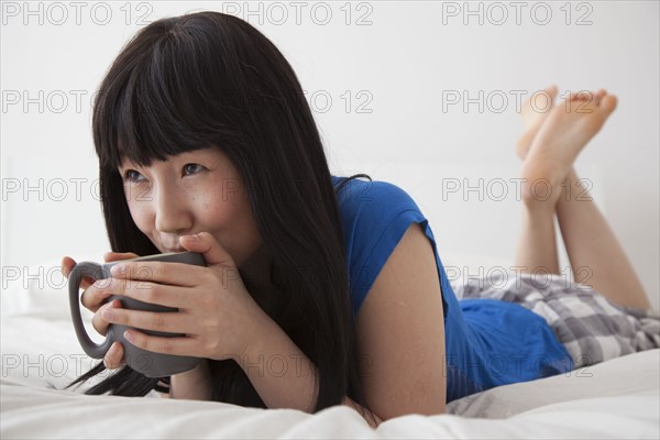 Chinese woman drinking cup of coffee on bed