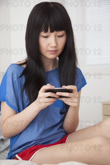 Chinese woman using cell phone on bed