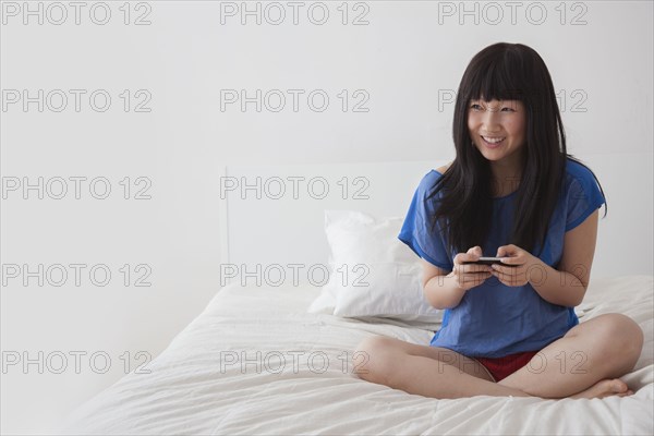 Chinese woman using cell phone on bed