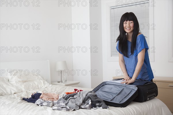 Chinese woman packing suitcase in bedroom