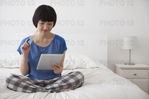 Chinese woman using tablet computer on bed